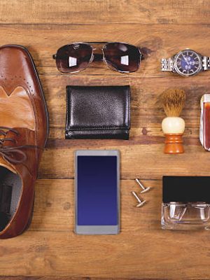 Variety of men's accessories organized in knolling arrangement.  Items include: dress shoes, tie, sunglasses, wallet, watch, shaving brush, cologne, and smart phone.  The items all lie on a wooden desk or table.   Men's personal accessories, clothing themes.  Father's Day.  Fashion.  Business.  Retail.